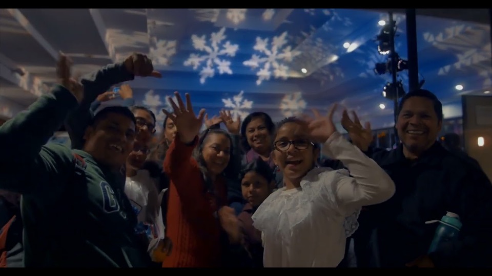 A crowd waving and celebrating at night under snowflake lights